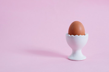 Brown egg in egg stand on a pink background.