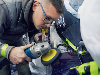 cheerful, young man with glasses polishes, primes and paints a car in the garage