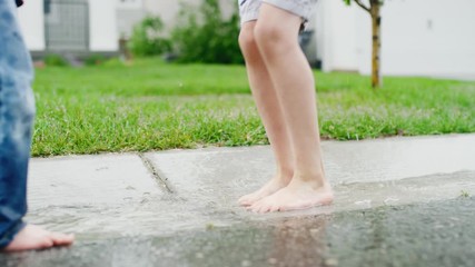 Close on 4 year old boy's feet splashing repeatedly in gutter on rainy day