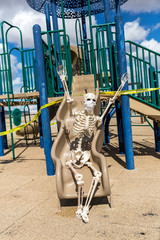 Adult skeleton sliding on childrens toys at an empty closed park on a nice day