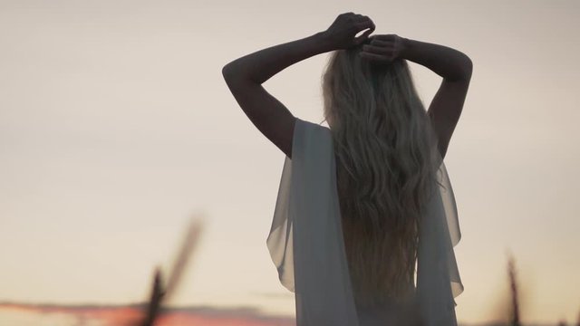 A soft and dreamy image of a young woman with a blown dress in grassy places at sunset. Young girl is free, inspiration. Young girl in a white image at sunset.