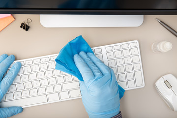 Hand with protective glove cleaning a keyboard with disinfectant. COVID-19 Coronavirus outbreak...