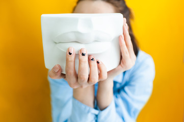 Woman holds plaster lips on a yellow background. concept pursuit of beauty and psychological...