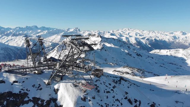 Orbit aerial over winter snowy mountain top ski tracks resort with skier people skiing. Drone video footage of Gondola lift cabin of ski-lift in the ski resort Val Thorens.