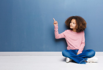 african american little girl standing and pointing to object on copy space, rear view sitting on the floor