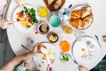 Family with young kids having healthy breakfast at home together. Flat-lay of plates with food and people hands over white textile round table background, top view. Preventive measures. Stay home.
