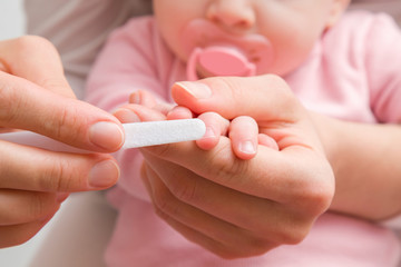 Young mother hands using white nail file for baby. Closeup. Front view.
