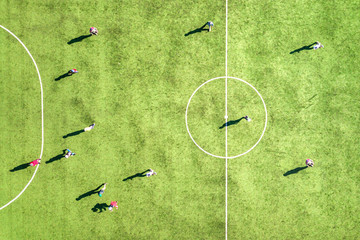 Top down aerial view of green football sports field and players playing football. Drone taken image of small unrecognizable sportsmen on grass covered stadium during sport activities.