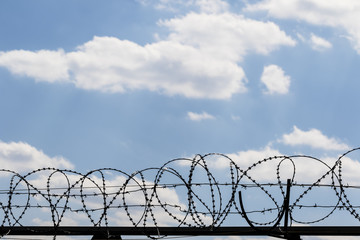 Black coiled barbed wire fence and blue sky with sunlit clouds