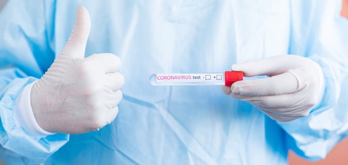 Hand holding a test tube with the inscription coronavirus test + - in front of you showing a positive result and class by raising the thumb up close-up
