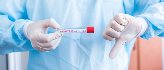 Hand holding a test tube with the inscription coronavirus test + - in front of him showing denial and discontent lowering the thumb down