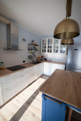 White, well lit scandi kitchen with blue island and double brass pendant lights. Vertical shot, side view.