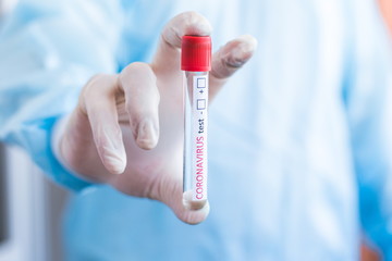 Fototapeta premium Doctor standing in a protective suit. holding a test tube in front of him with the inscription coronavirus test + - close-up