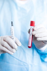 Doctor standing in a protective suit. Holding a close-up medical tube containing a blood sample for testing COVID-19 with a syringe. Vertical photo