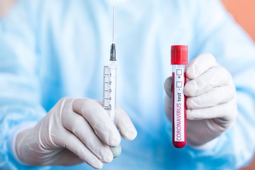 Doctor standing in a protective suit. Holding a medical test tube containing a blood sample for COVID-19 testing with a close-up syringe