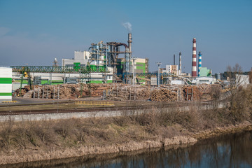 Fototapeta premium pipes of woodworking enterprise plant sawmill near river. Air pollution concept. Industrial landscape environmental pollution waste of thermal power plant