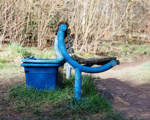 Blue rubbish bin for dog's litter  is behind the blue bench in the park