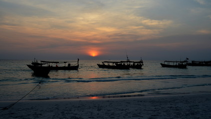Typical cambodian wooden boats anchored on the coast with the pink sunset at the back
