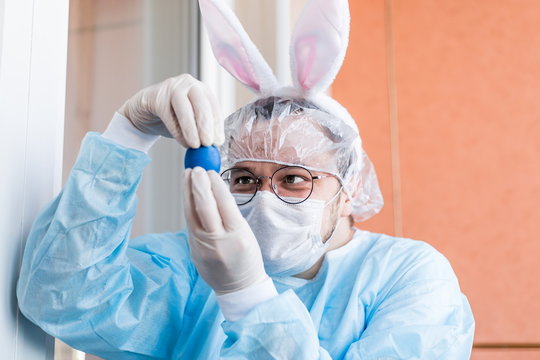 Easter hare dressed in a protective suit against viruses. Looking at an Easter egg during the COVID-19 pandemic