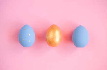 Fototapeta na wymiar Gold and blue easter eggs on pink background.