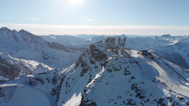Orbit aerial over winter snowy mountain top ski tracks resort with skier people skiing. Drone video footage of Gondola lift cabin of ski-lift in the ski resort Val Thorens.