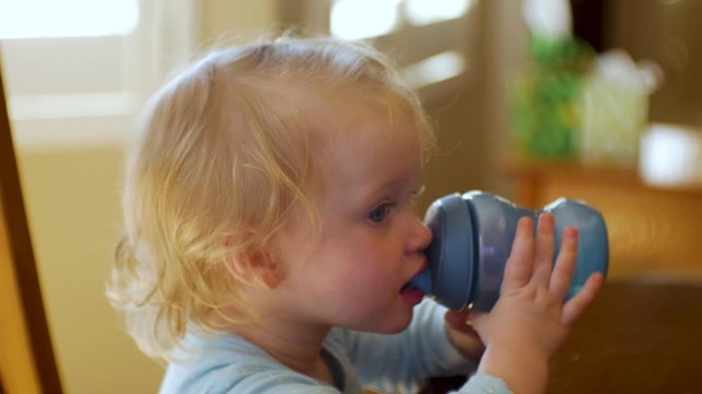 Adorable female toddler drinks water, joice or milk from her sippy cup - close up