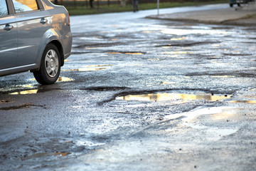 Close up of car wheel on a road in very bad condition with big potholes full of dirty rain water...