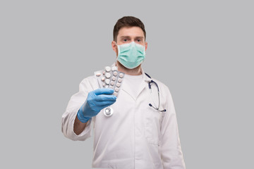 Man Doctor Showing Pills Wearing Medical Mask. Doctor Holding Tablets. Corona Virus Concept.
