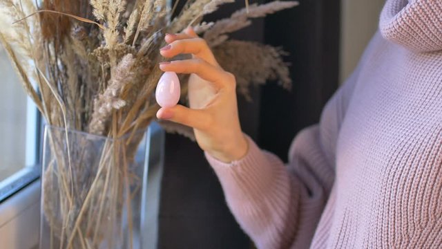 Girl is holding yoni egg made from rose quartz stone on spikelets background. Female health concept, vumfit, imbuilding or meditation