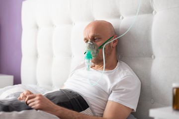 Man breathing through oxygen mask in bed. Covid-19 patient.