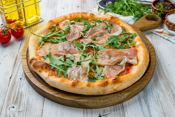 Pizza with Parma ham and arugula on white wooden table