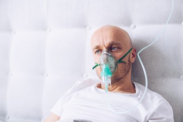Man breathing through oxygen mask in bed. Covid-19 patient.
