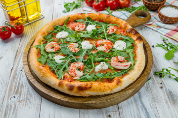 Pizza with arugula and shrimp on white wooden table