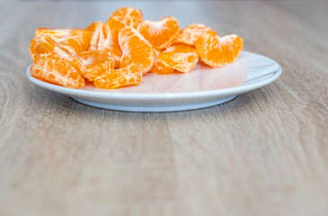 Fototapeta na wymiar Pealed mandarin peaces on white plate, wooden desk surface