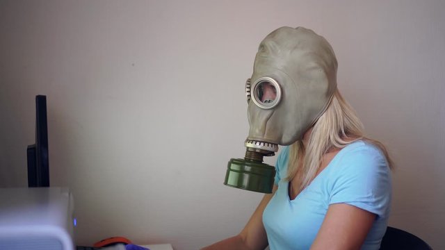A woman in a gas mask or respirator works at home on a computer. Coronovirus Prevention