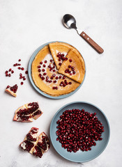 Grains of peeled pomegranate lie in a plate. Pancakes with pomegranate and condensed milk lie on a plate. View from above. Close-up.