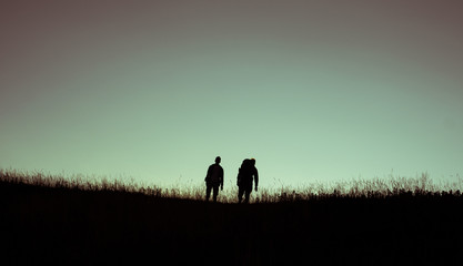 Naklejka na ściany i meble two friends travellers on hill during sunset silhouette