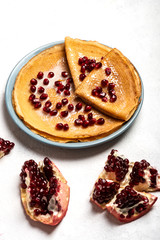 Pancakes with pomegranate and condensed milk lie on a plate. Close-up.