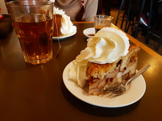 high Dutch apple pie with plenty of whipped cream on a brown wooden table with a cup of hot tea in winter