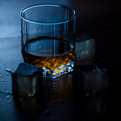 glass of water on blue background with ice whisky and gin
