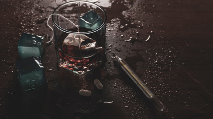 glass of tea or whiskey with pills and thermometer