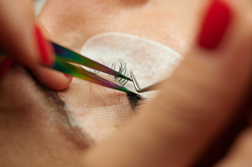 Eyelash extension in process, hands holding tweezers and gluing eyelash close up view