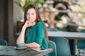 Beautiful elegant girl having breakfast at outdoor cafe. Happy young urban woman drinking coffee