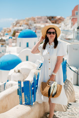 girl in a white dress with glasses on a background of white houses with blue roofs in Santorini