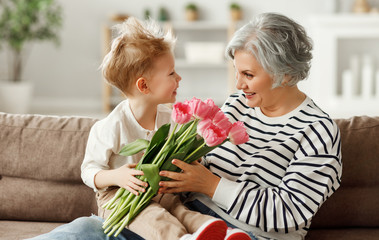 Cheerful little boy giving flowers to grandmother.
