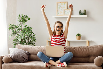 Glad woman celebrating good news while working on laptop at home.