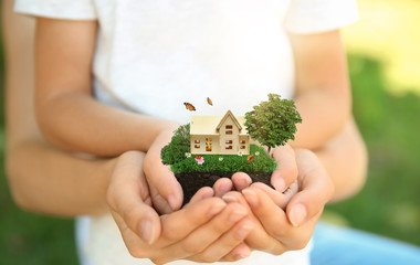 Woman and her child holding their dream house with beautiful green lawn on sunny day, closeup