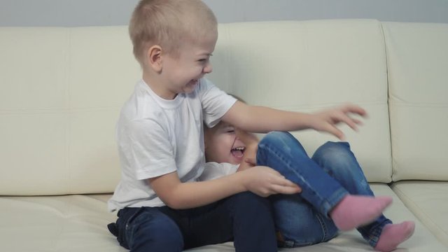 children play tickle each other happy family. boy and little girl play indoors on the couch. brother and sister have fun and relax happy lifestyle family