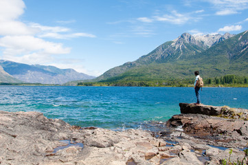 Fototapeta na wymiar A man with a brown backpack standing and looking the mountains at the shore of Epuyen Lake. Photo taken at the Epuyen Provincial Park in the Cushamen department, Chubut province, Argentina.