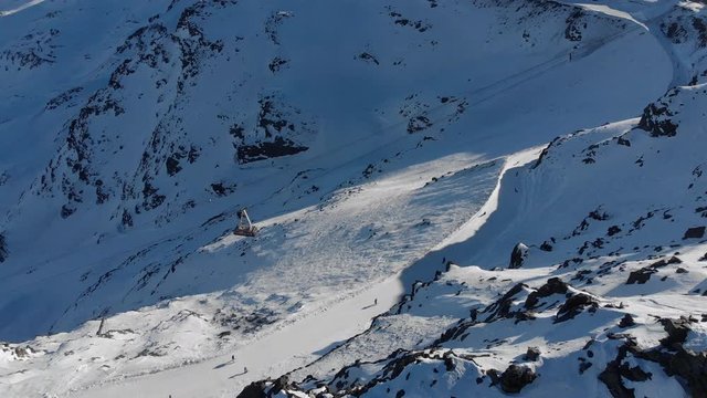 Orbit aerial over winter snowy mountain top ski tracks resort with skier people skiing. Drone video footage of Gondola lift cabin of ski-lift in the ski resort Val Thorens.